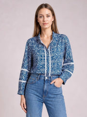 Model wears a blue-and-white printed mock neck long sleeve blouse with a relaxed silhouette, patterned cuffs, and a straight front placket, posing with one hand in her jeans pocket.