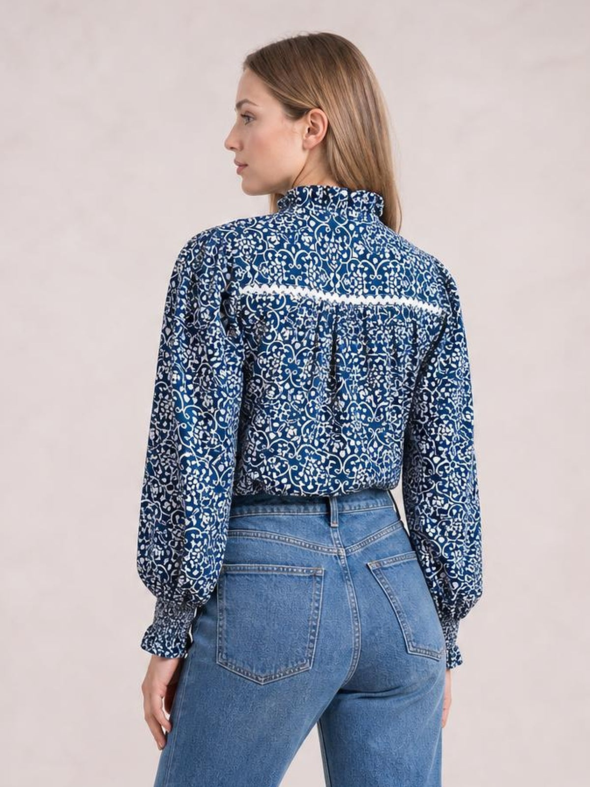 Model shown from the back wearing a blue and white printed mock neck long sleeve blouse with a relaxed silhouette and gathered cuffs.