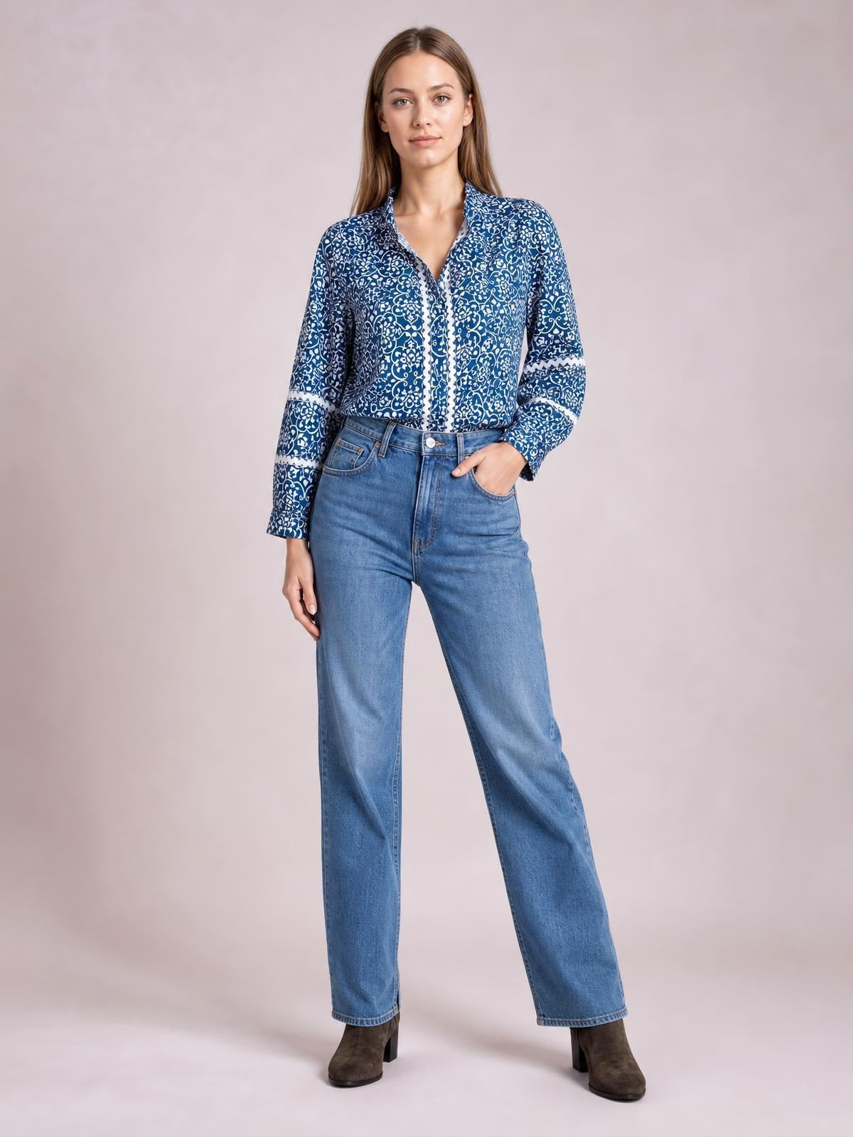 A model poses in a blue-and-white printed long-sleeve blouse with a short mock neck, button front, relaxed silhouette, and one hand in her jeans pocket.