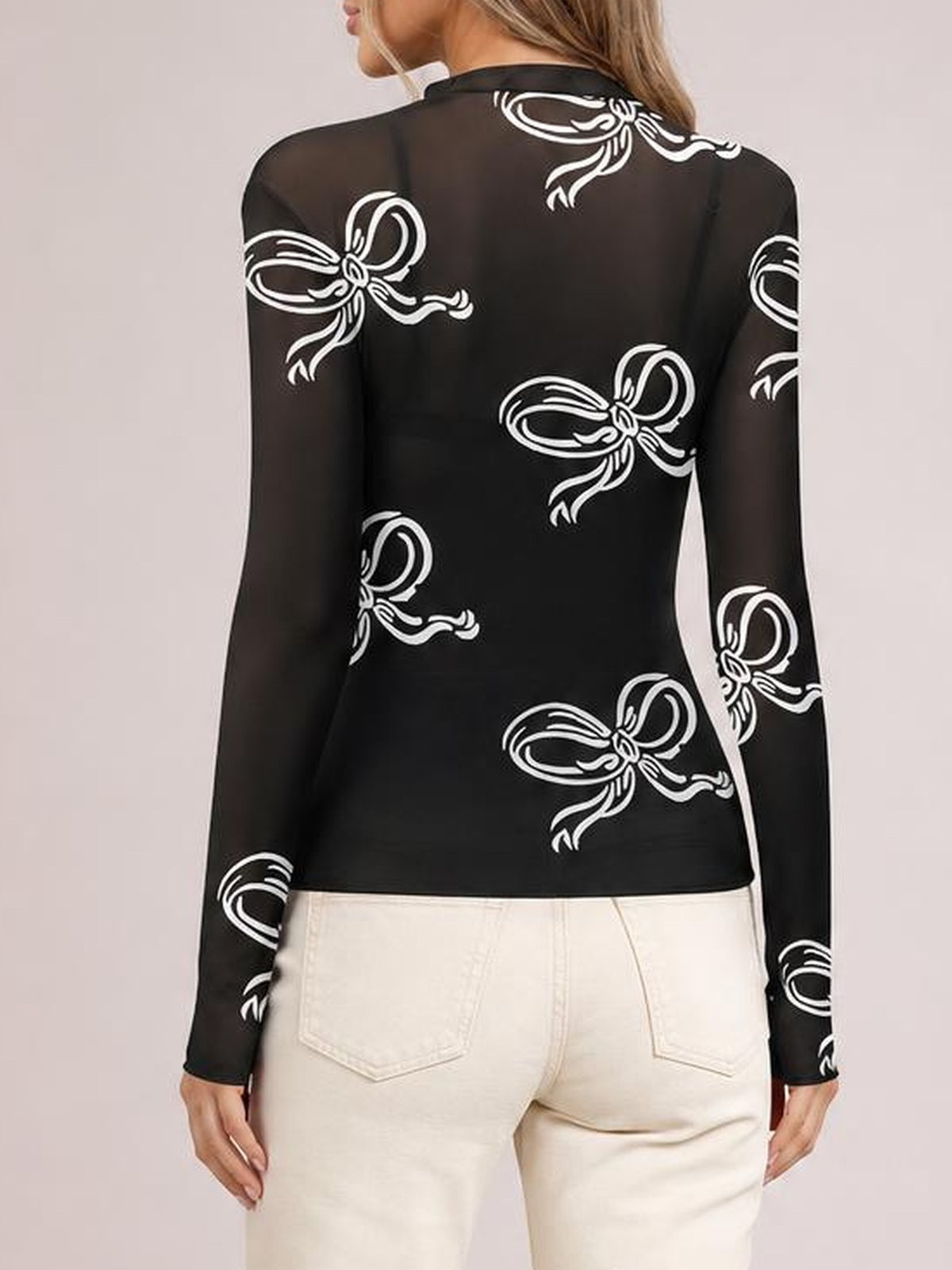 Model shown from the back wears a fitted black sheer mesh T-shirt with a mock neck, long sleeves, white bow print, and straight hem.
