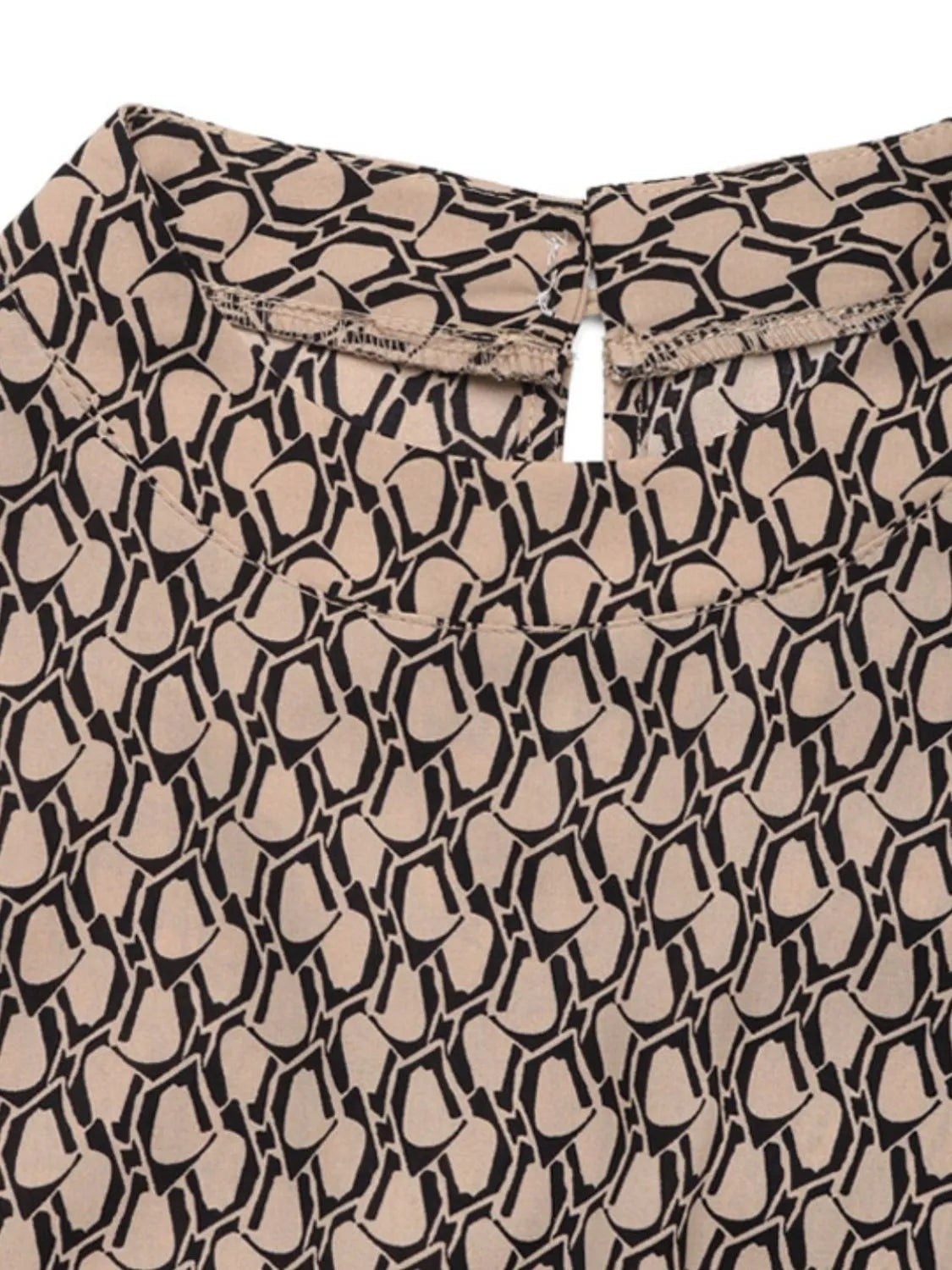 Close-up of the printed mock neck jumpsuit in beige and black, showing its bold geometric pattern, high neckline, and neatly finished upper construction.