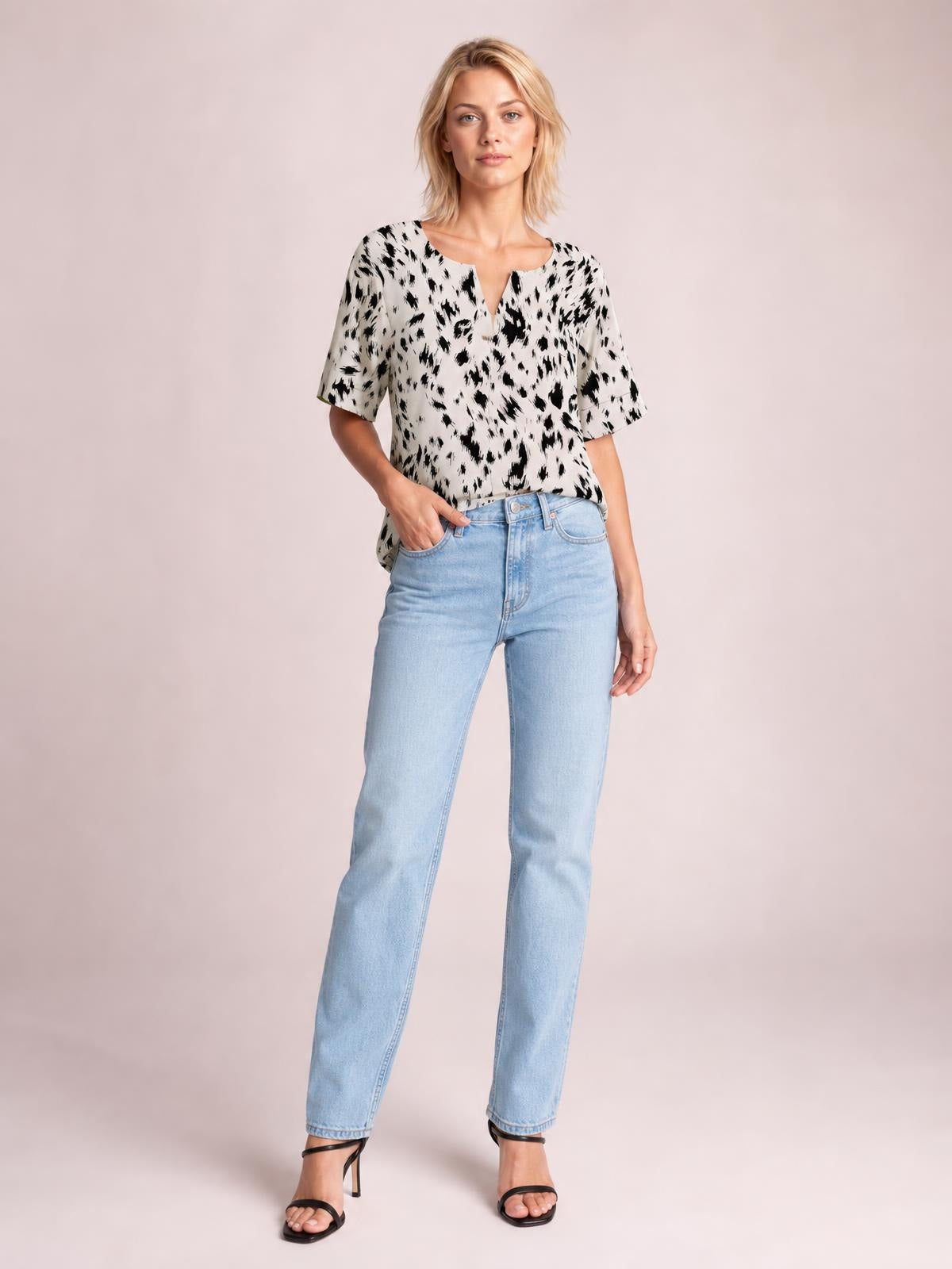 A model stands with one hand in her jeans pocket, wearing a chic white-and-black printed blouse with a notched neck, half sleeves, and a relaxed regular-length silhouette.
