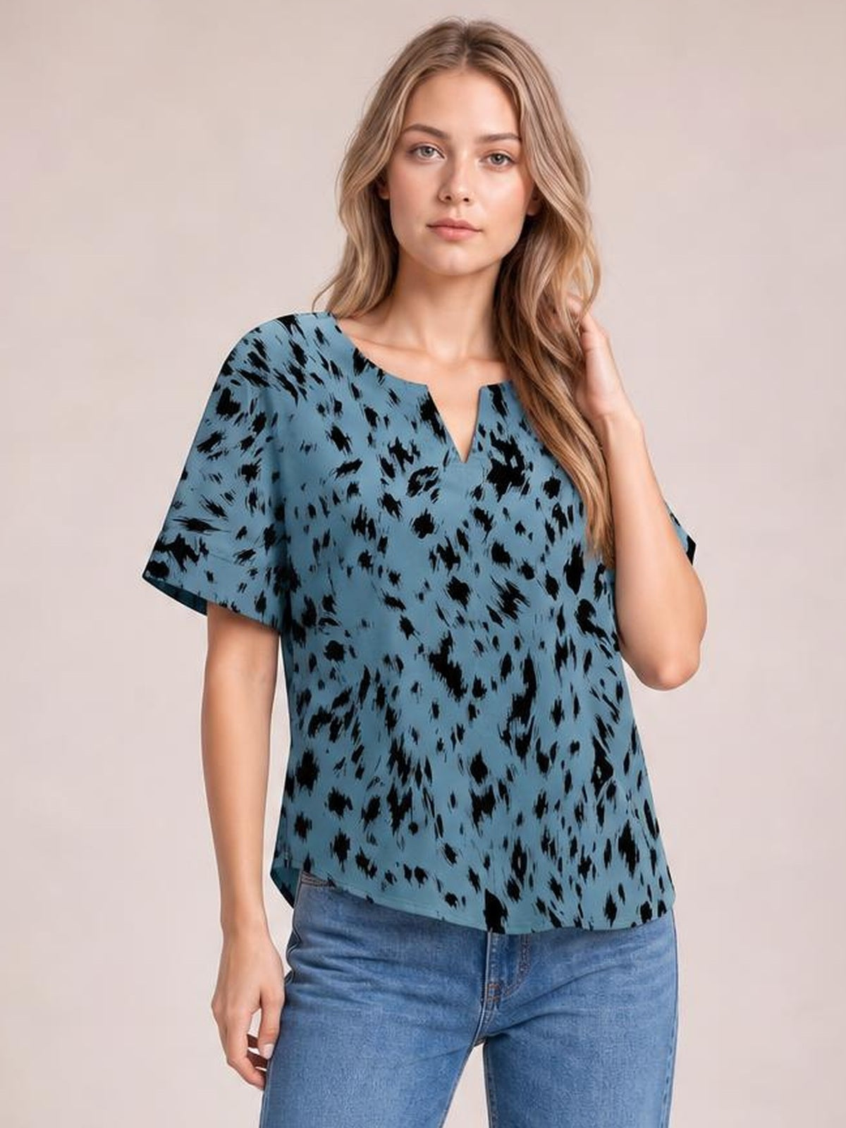 Model wearing a blue printed blouse with black abstract spots, a notched neckline, loose regular silhouette, and short half sleeves.