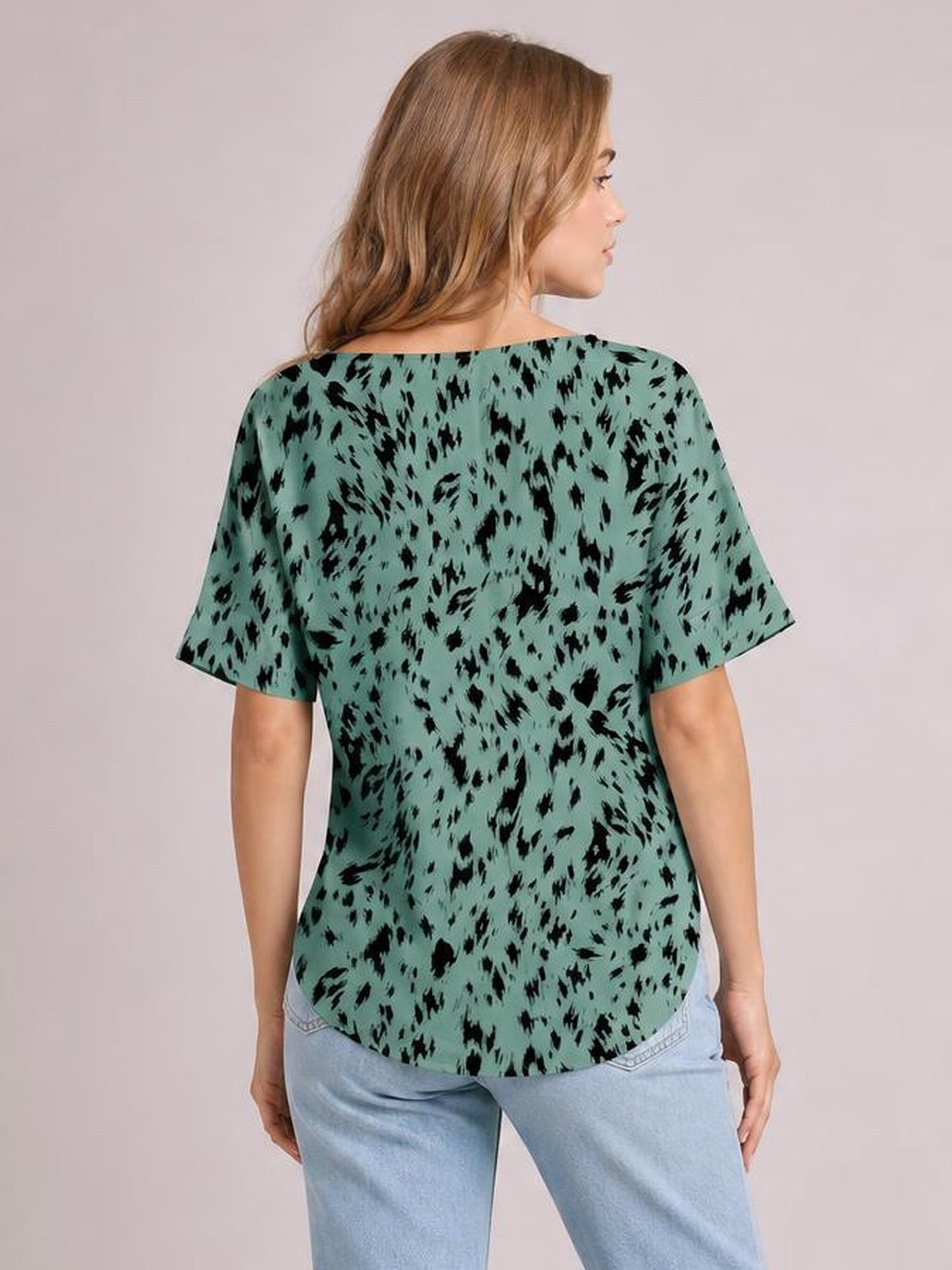 Model shown from the back wears a mint-green printed blouse with black abstract motifs, short sleeves, a relaxed regular silhouette, and a curved hem.
