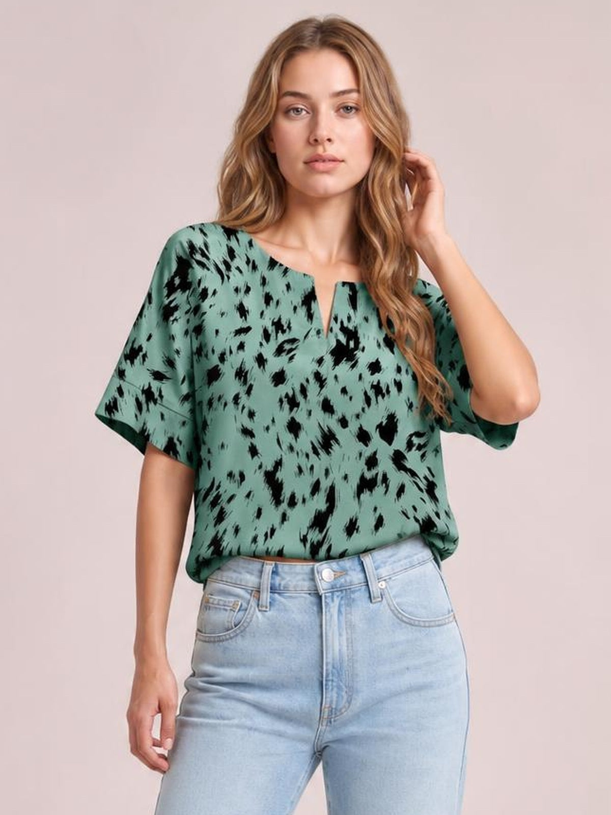 Model wearing a mint green printed blouse with a notched neck, loose regular silhouette, and short half sleeves, posing with one hand in her hair.
