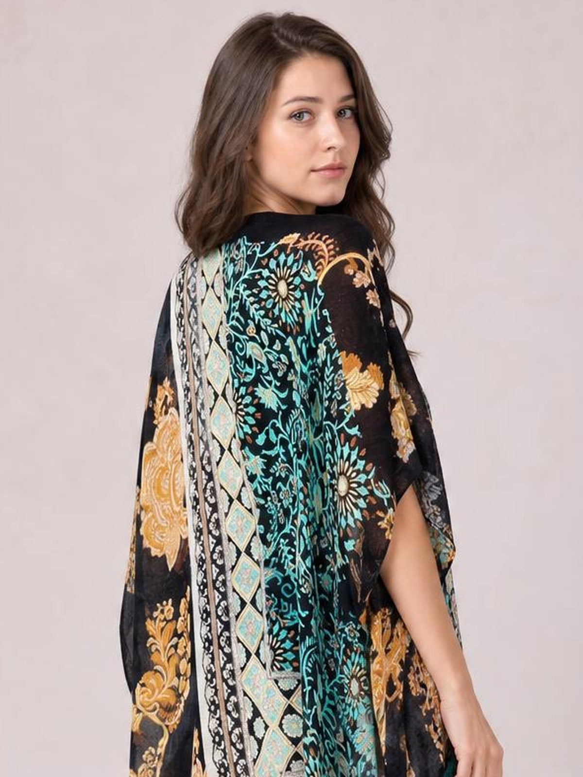 Model looks over her shoulder wearing a black printed open front cover-up with turquoise and gold floral motifs, loose draped silhouette, and flowing sleeves.