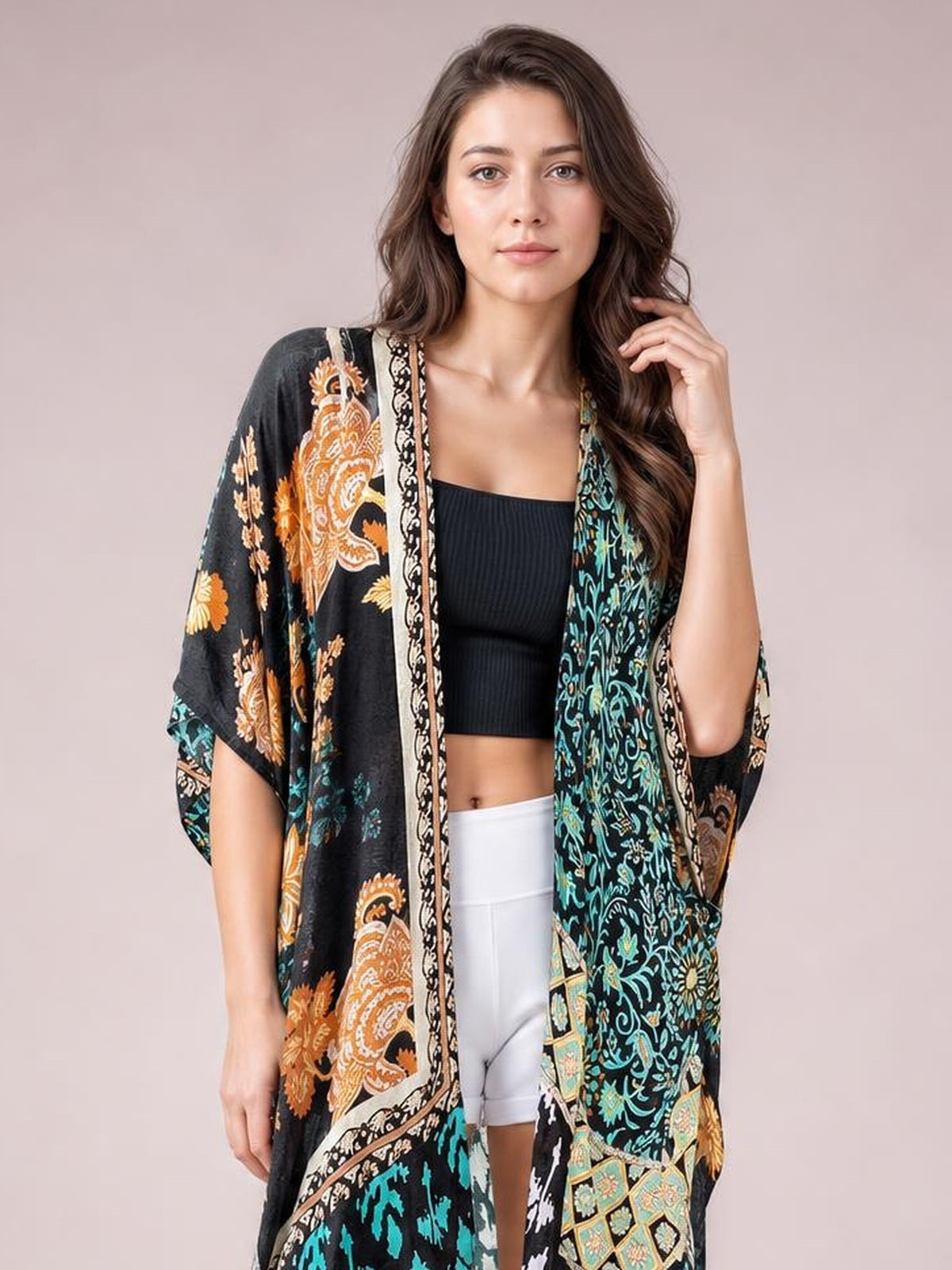 Model poses in a black printed open front cover-up with colorful floral and paisley patterns, relaxed draped silhouette, and wide three-quarter sleeves.