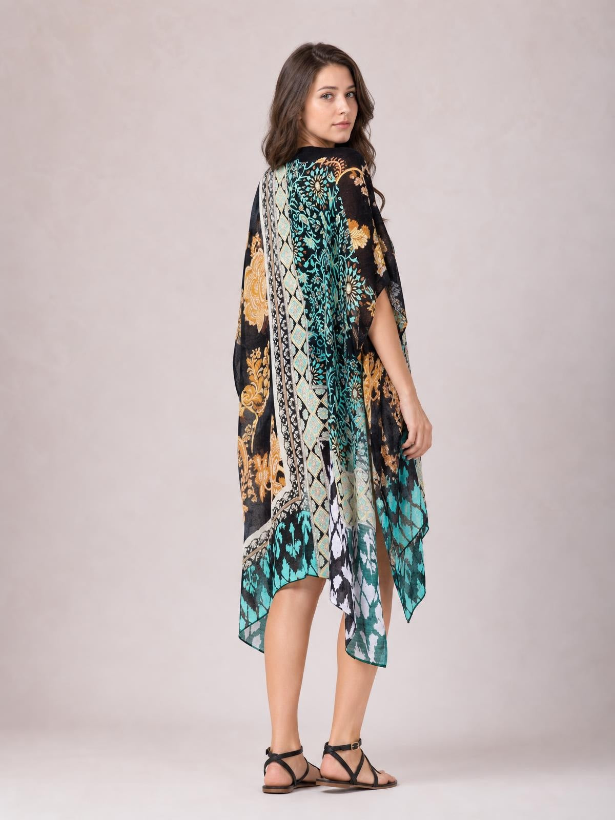 Model in a printed open front cover-up with a flowing oversized silhouette, black base, turquoise and gold floral patterns, and asymmetrical hem.