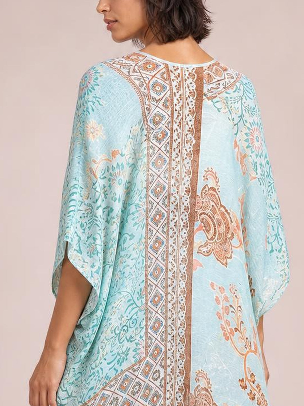 A model shown from behind wears a light blue printed open front cover-up with floral and geometric patterns, a relaxed silhouette, and loose three-quarter sleeves.