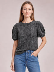Model wearing a black printed round-neck short-sleeve blouse with a relaxed straight silhouette and gently gathered sleeves, posed with one hand in her jeans pocket.
