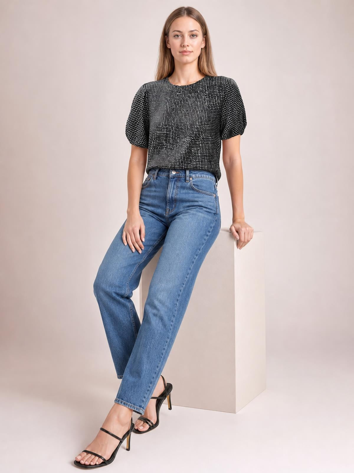 A model sits in a black-and-white printed blouse with a round neckline, short sleeves, and a relaxed straight silhouette, paired with blue jeans.