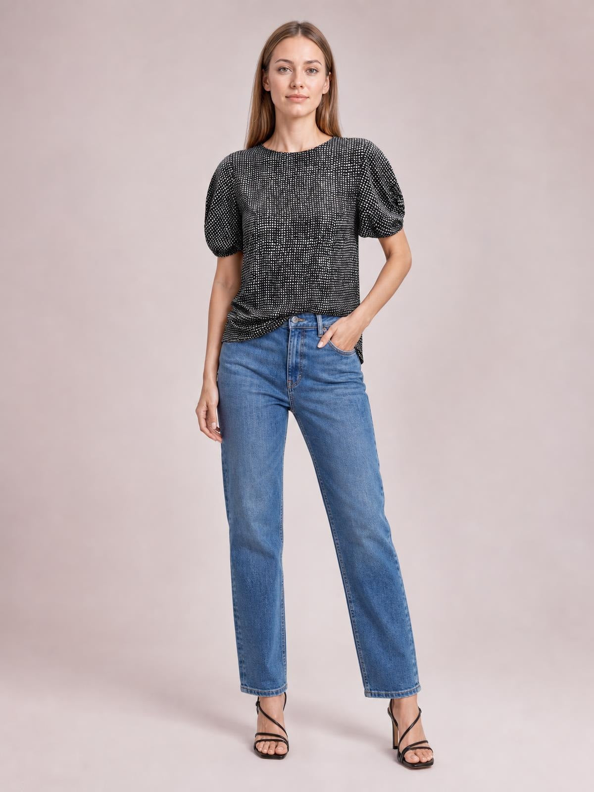 Model wears a black printed round-neck short-sleeve blouse with a relaxed silhouette, gently gathered sleeves, and a draped hem, posing with one hand in her jeans pocket.