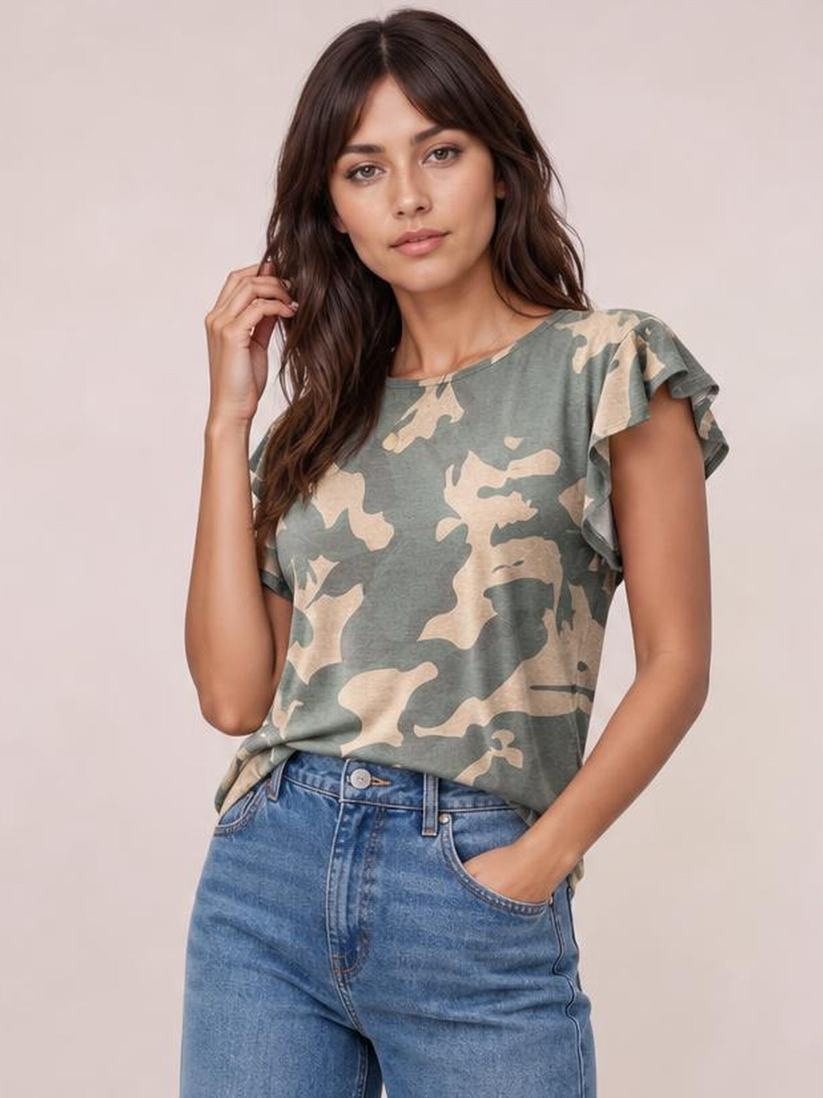 Model wearing a green and beige printed round neck short sleeve T-shirt with a relaxed silhouette and ruffled sleeve details, posing with one hand in her jeans pocket.