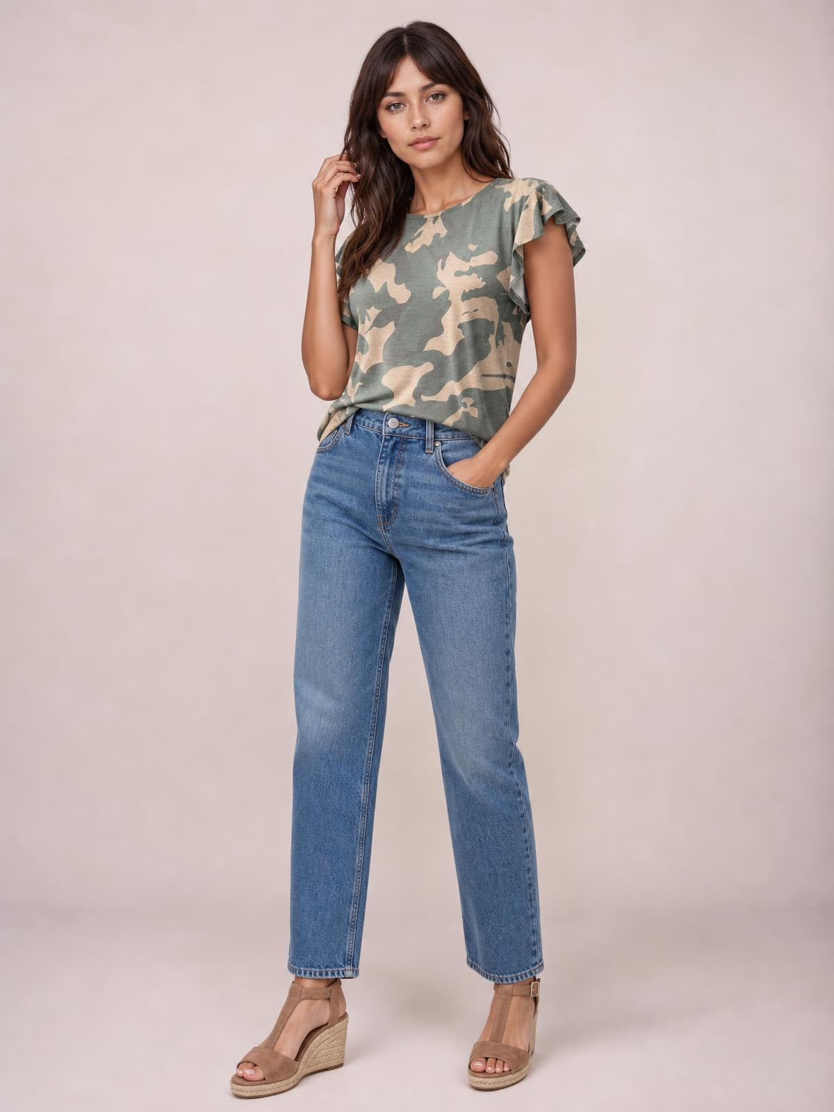 A model poses with one hand in her jeans pocket, wearing a green and beige printed round-neck short-sleeve T-shirt with a fitted silhouette and flutter sleeves.