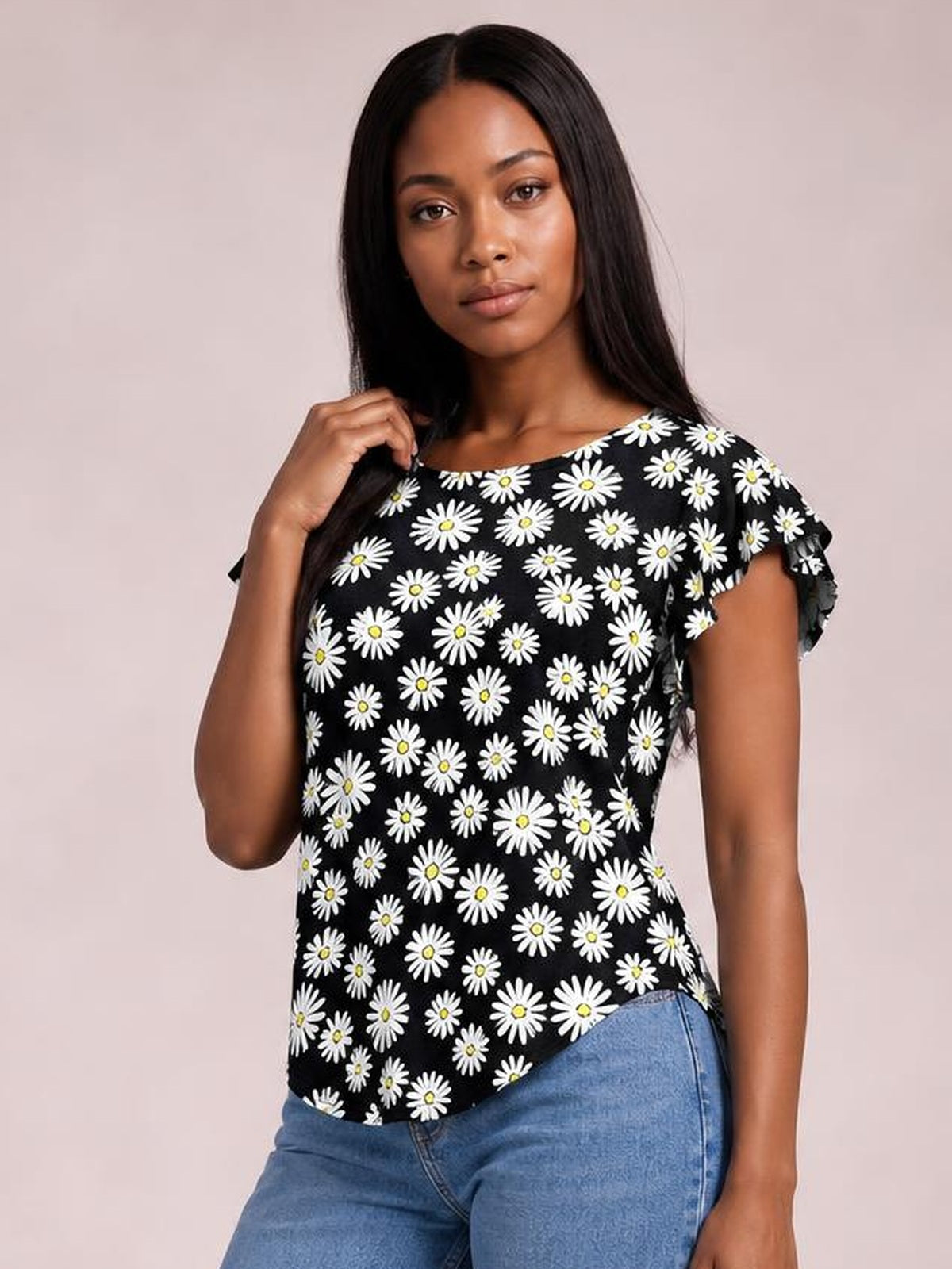 Model wearing a black floral printed round neck short sleeve T-shirt with white daisies, a relaxed silhouette, curved hem, and flutter sleeve edges.