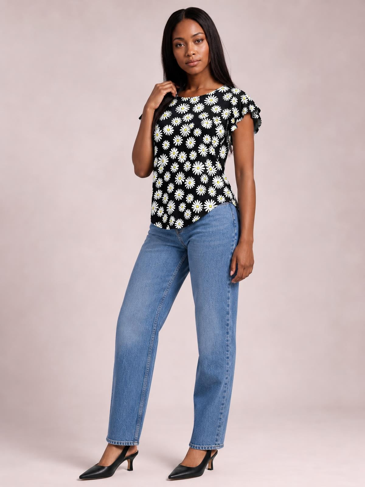 Model wears a black printed round-neck short-sleeve T-shirt with white daisy pattern and a relaxed, gently shaped silhouette, posing with one hand near her hair.
