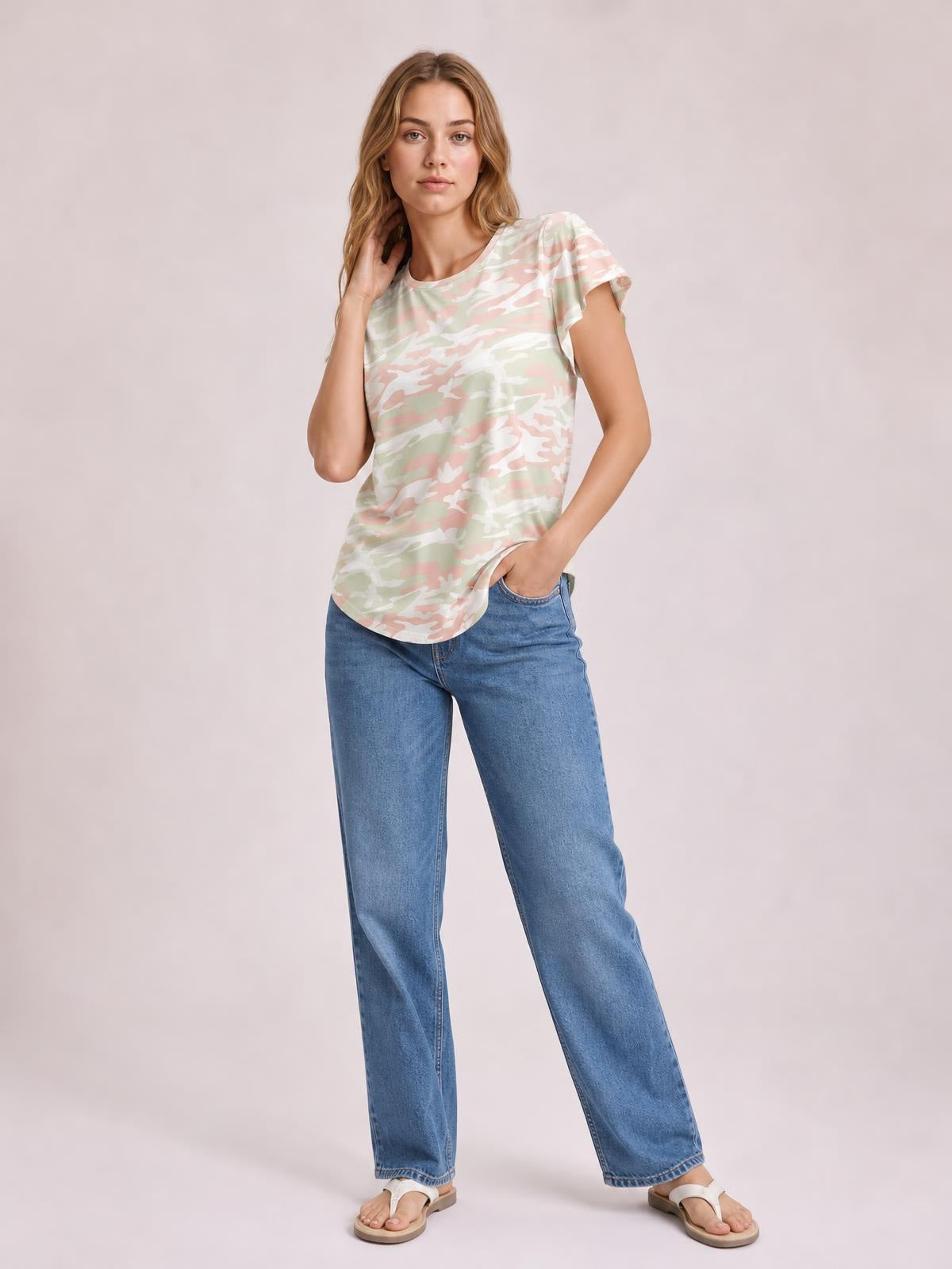 Model poses in a pastel camouflage printed round-neck short-sleeve T-shirt with a relaxed silhouette and curved hem, paired with jeans.