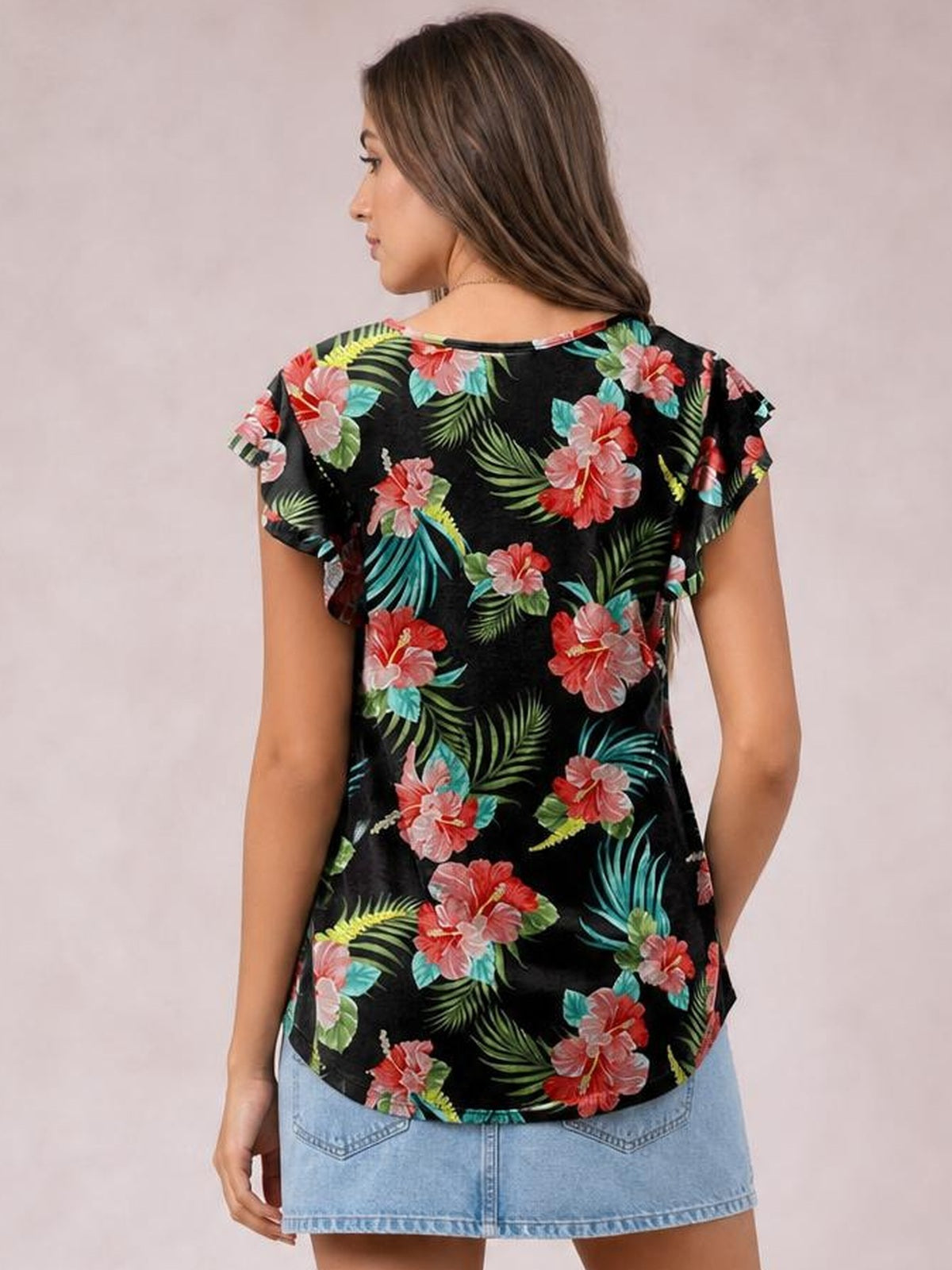 A woman poses from the back in a black printed round neck short sleeve T-shirt with colorful tropical flowers, a relaxed silhouette, and a curved hem.