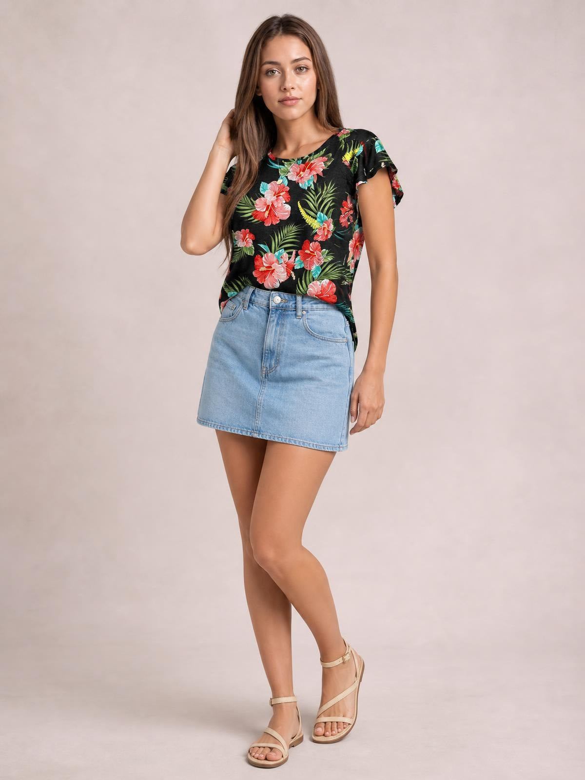 Model poses in a black printed round neck short sleeve T-shirt with colorful floral and leaf motifs, a relaxed silhouette, and gently ruffled sleeve edges.