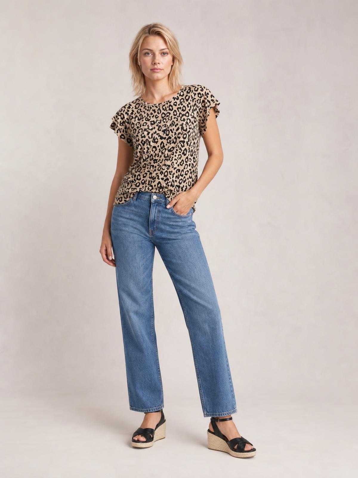 Model wears a tan and black printed round-neck short-sleeve T-shirt with a relaxed silhouette and ruffled sleeve edges, paired with blue jeans.