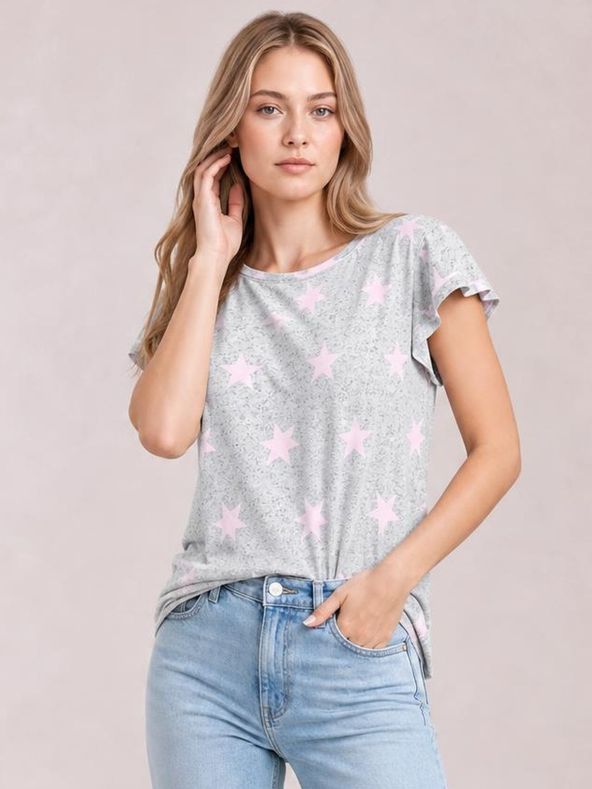 Model wears a light gray printed round neck short sleeve T-shirt with pink stars, a relaxed silhouette and slightly draped hem, posing with one hand in her jeans pocket.