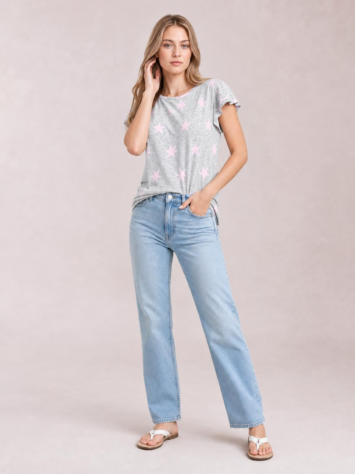 Model wears a light gray printed round neck short sleeve T-shirt with pink stars and a relaxed silhouette, posing with one hand in her jeans pocket.