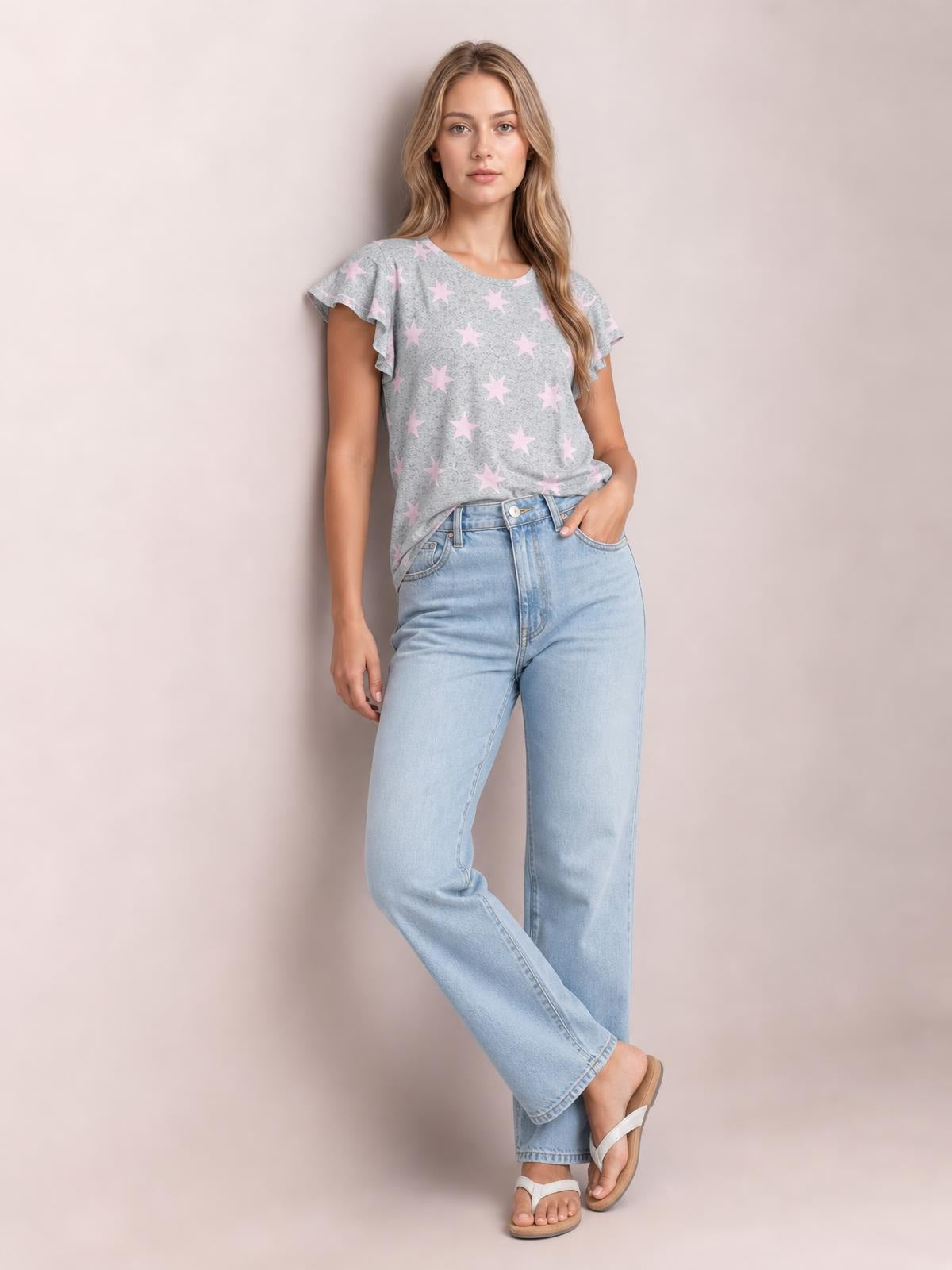 Model wears a gray printed round neck short sleeve T-shirt with pink stars and flutter sleeve details in a relaxed silhouette, paired with light-wash jeans.