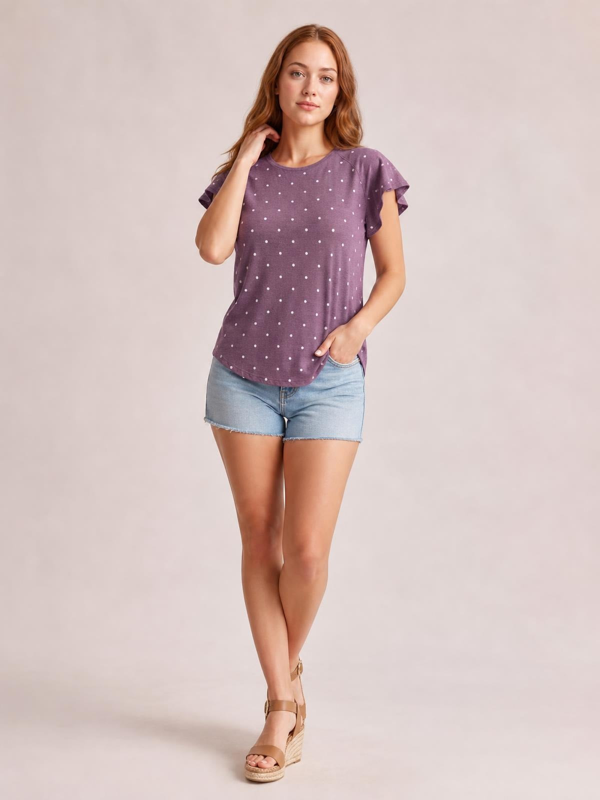 Model wears a purple printed round neck short sleeve T-shirt with white polka dots, a relaxed silhouette, and subtly ruffled sleeve edges.