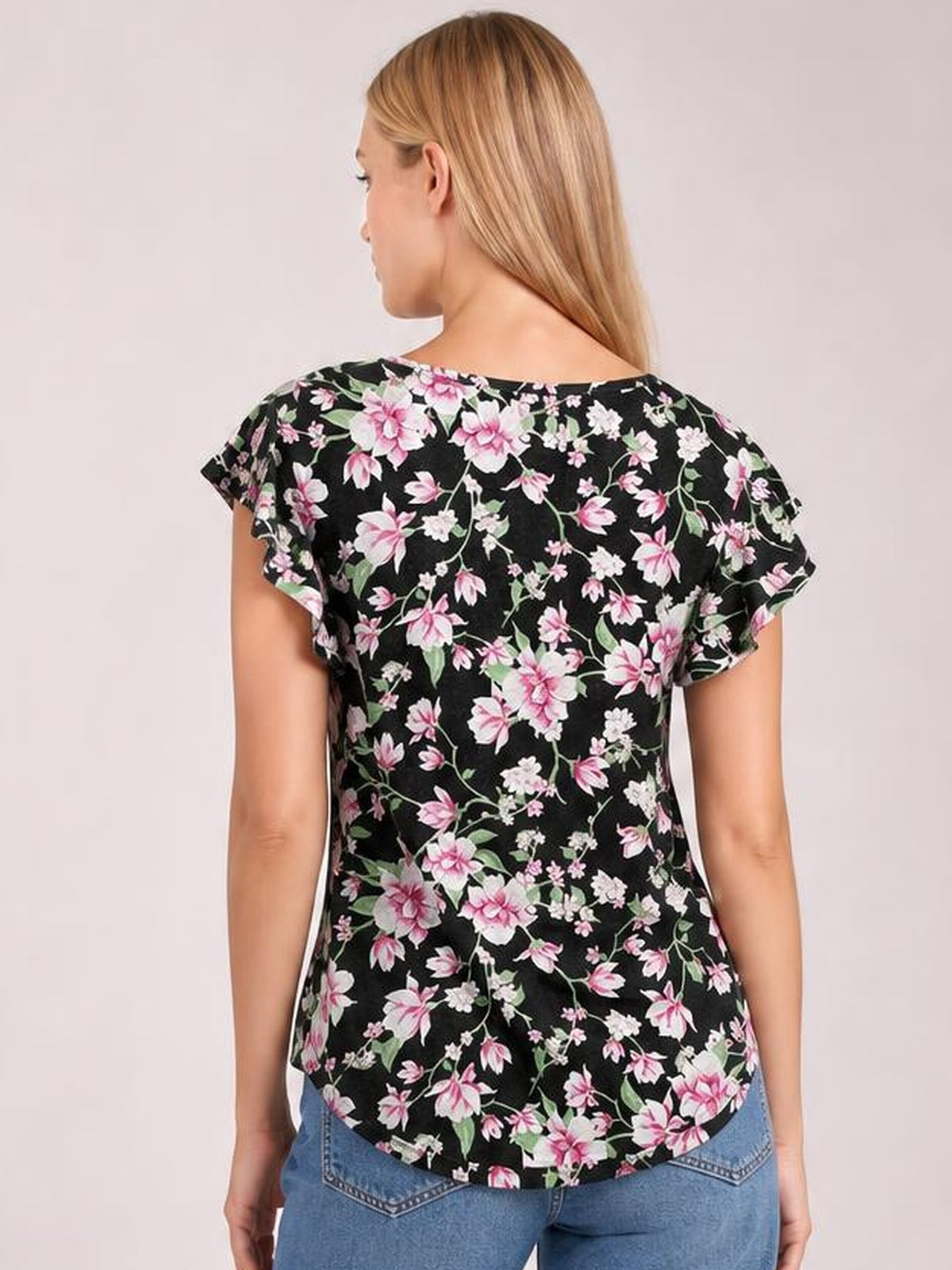 A model faces away wearing a black printed round neck short sleeve T-shirt with pink floral pattern, relaxed silhouette, and curved hem.