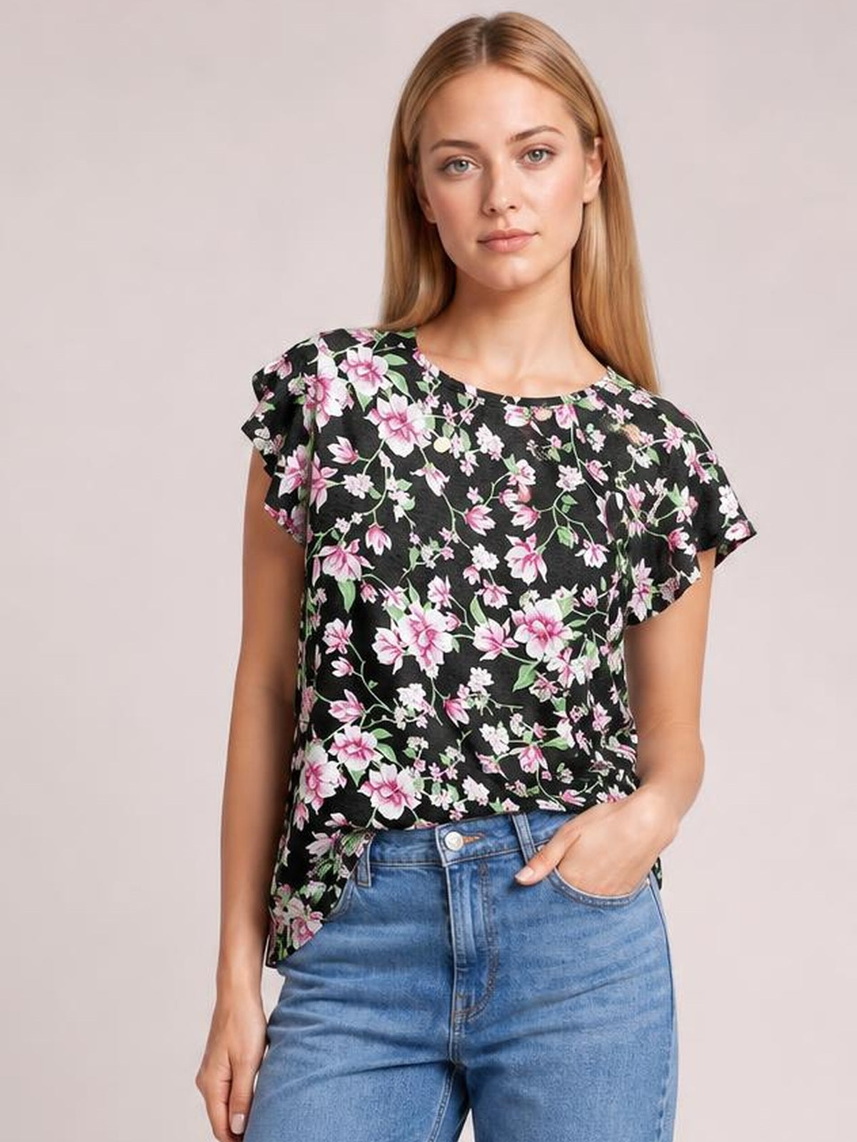 Model wearing a black printed round neck short sleeve T-shirt with pink and white floral detailing, relaxed silhouette, and one hand in her jeans pocket.