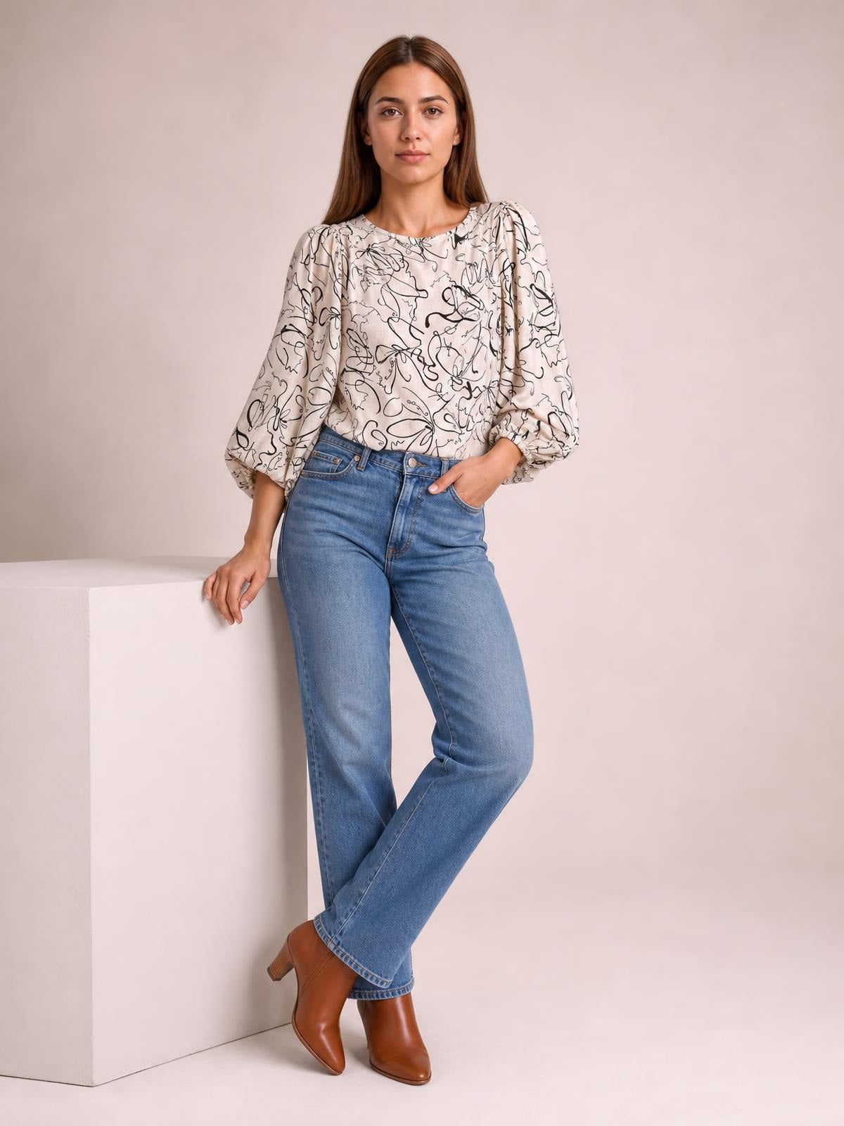 Model wearing a pale pink printed round-neck blouse with black abstract florals, gathered three-quarter sleeves, and a relaxed silhouette, standing with one hand in her pocket.
