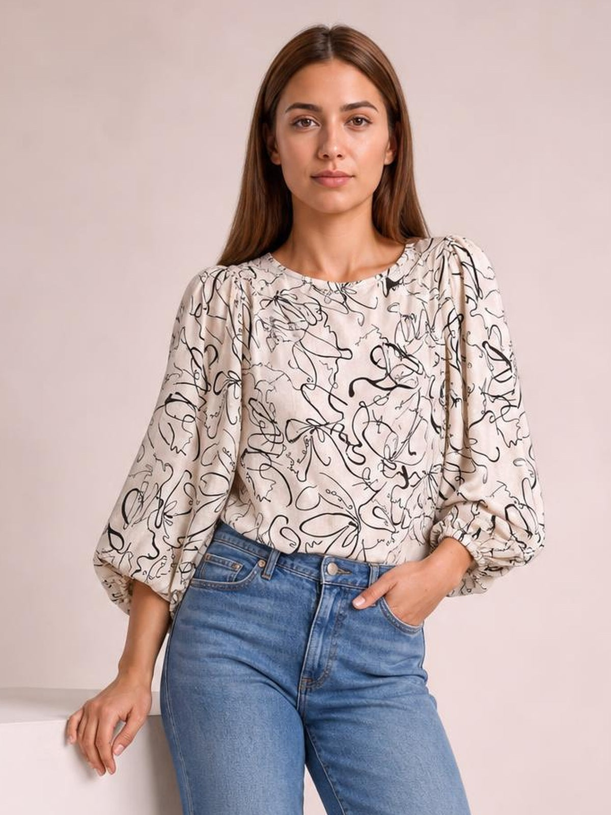 Model wears a cream printed blouse with a round neck, gathered shoulders, voluminous three-quarter sleeves, and elastic cuffs in a relaxed silhouette.