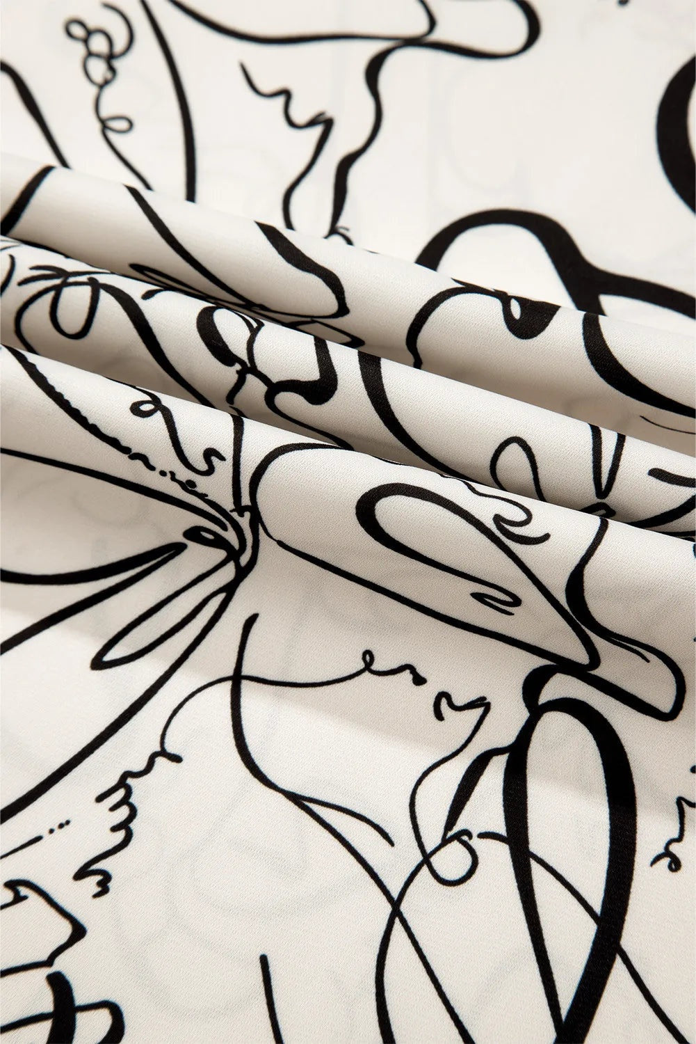 Cream printed blouse fabric features bold black abstract line-art motifs and a softly draped, opaque polyester texture.