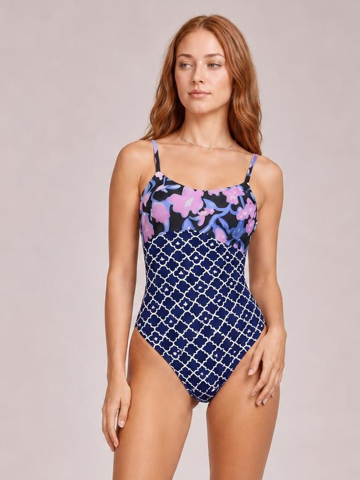 Model poses in a printed spaghetti strap one-piece swimsuit with a sweetheart neckline, navy geometric lower pattern, and pink and lavender floral bodice.