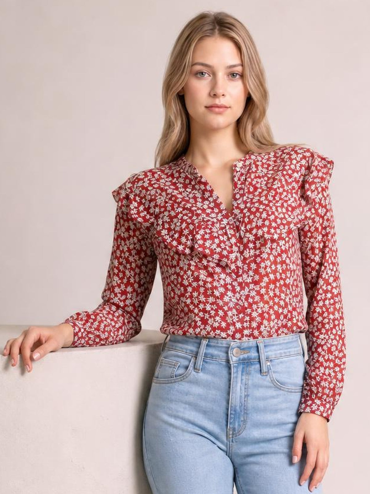 Model wears a red floral printed long-sleeve blouse with a statement collar, button front, and fitted silhouette while resting one hand on a ledge.