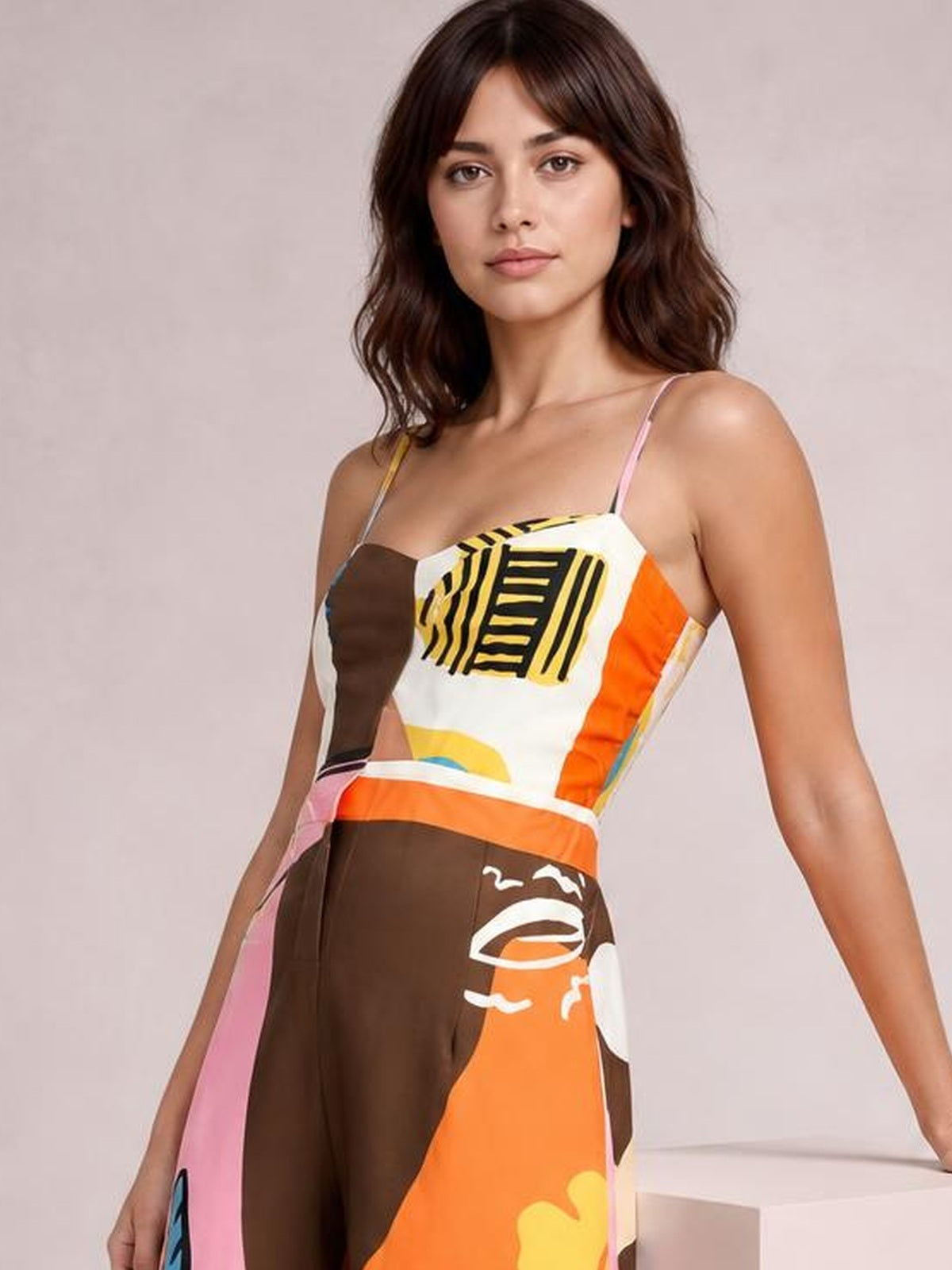 Model stands in a printed sweetheart-neck jumpsuit with thin straps, a fitted multicolor bodice, and wide brown, orange, pink, and yellow legs.