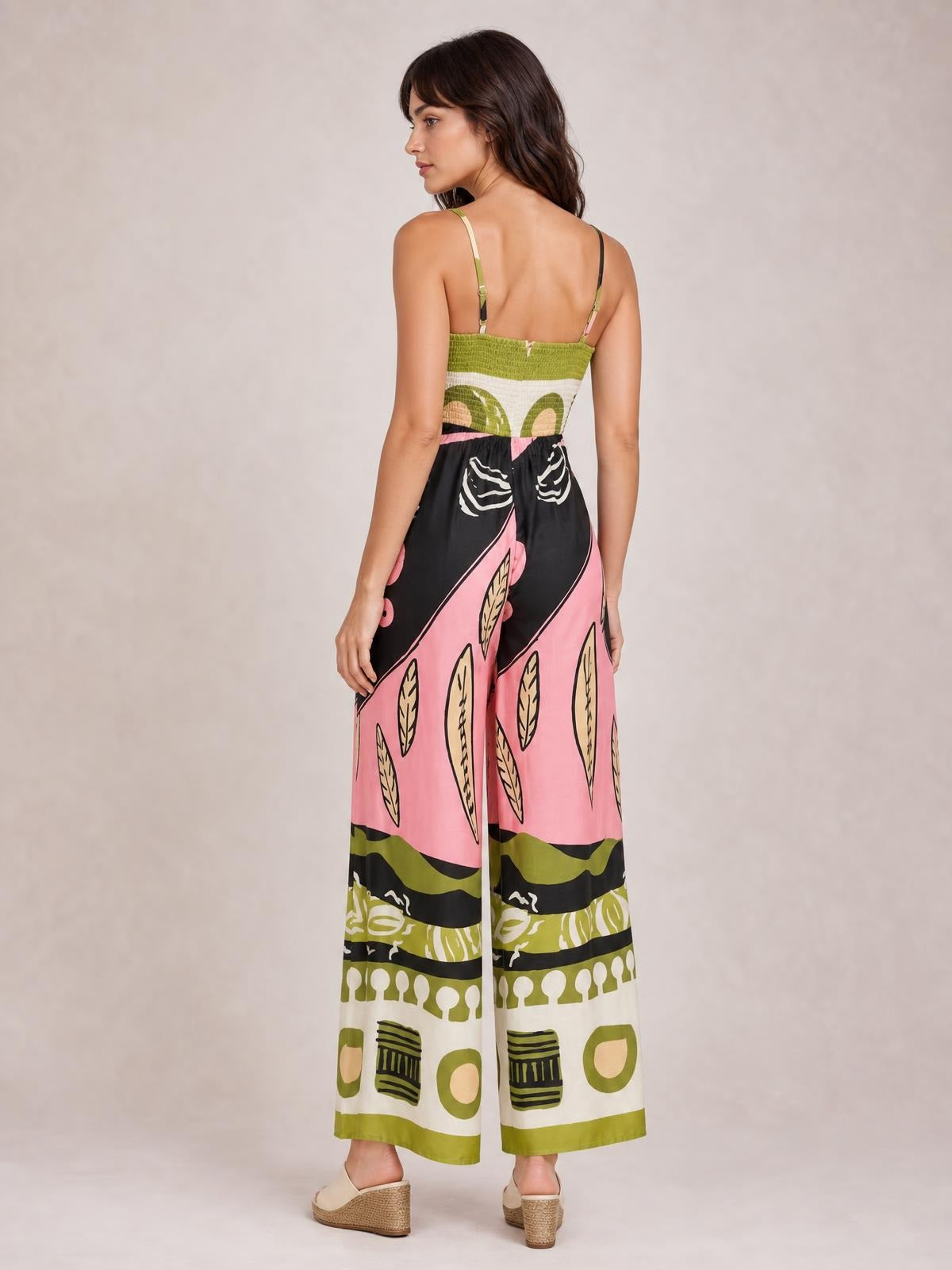 Model stands turned away in a printed jumpsuit with thin straps, a smocked back, and wide pink, black, green, and cream legs.