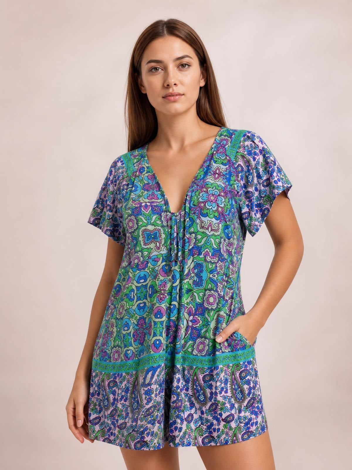 Model wearing a colorful printed tie-front romper with short sleeves, a relaxed silhouette, V-neckline, and loose shorts in blue, green, and purple.