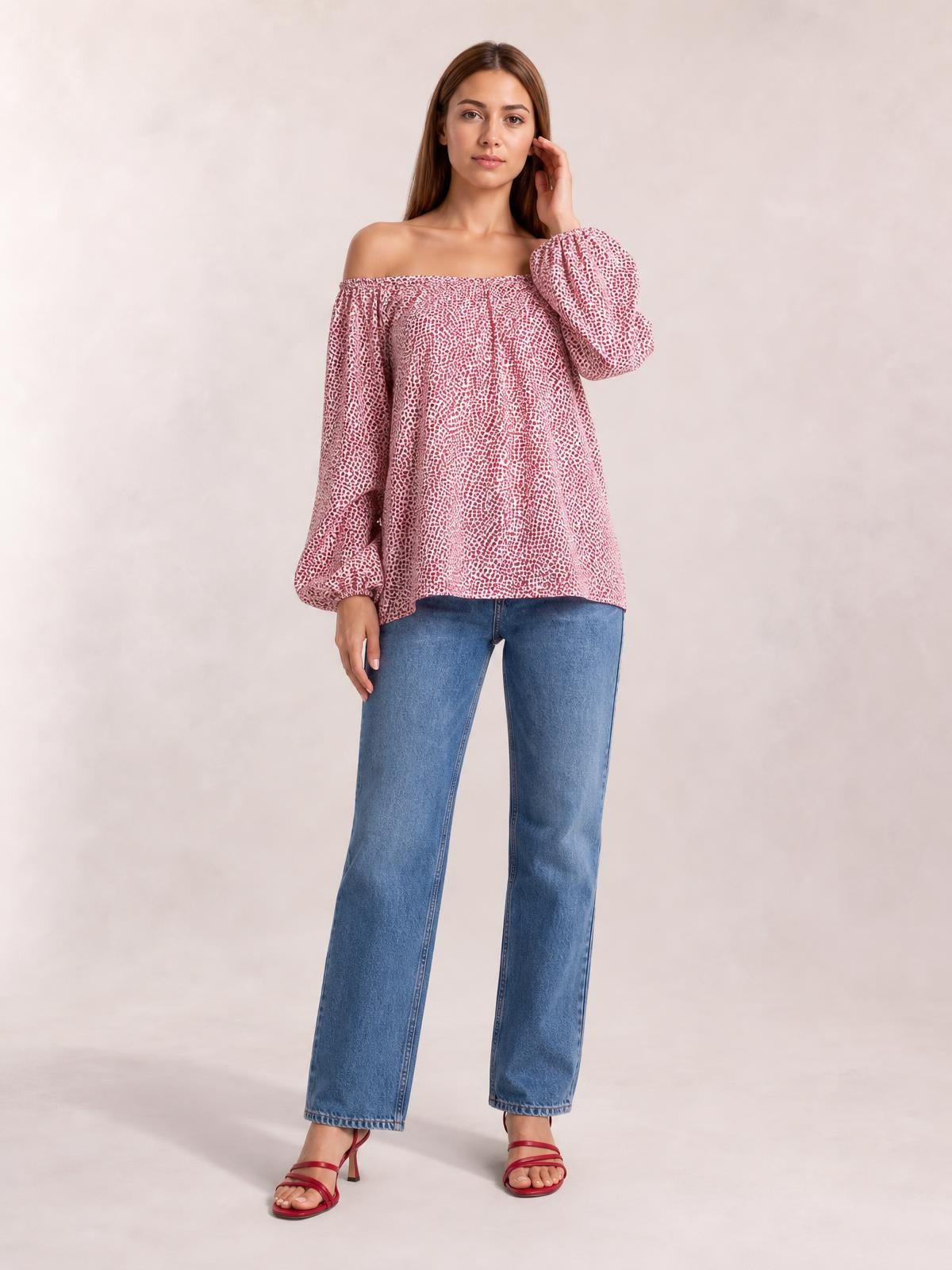 Model wears a pink-and-white printed blouse with an off-shoulder neckline, long balloon sleeves, and a relaxed long silhouette while touching her hair.
