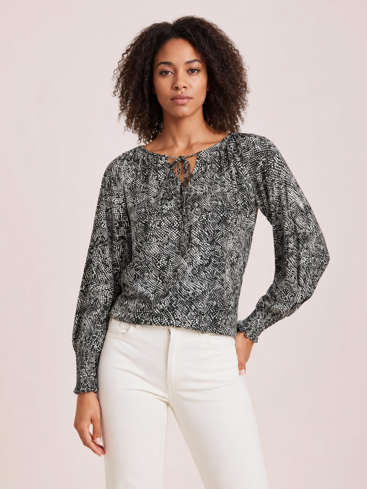 Model poses in a black-and-white printed blouse with a tied neckline, voluminous lantern sleeves, gathered cuffs, and a relaxed silhouette.