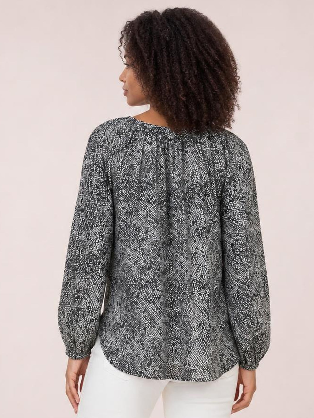 Model viewed from behind wearing a black-and-white printed blouse with a loose silhouette, long lantern sleeves, and gathered cuffs.