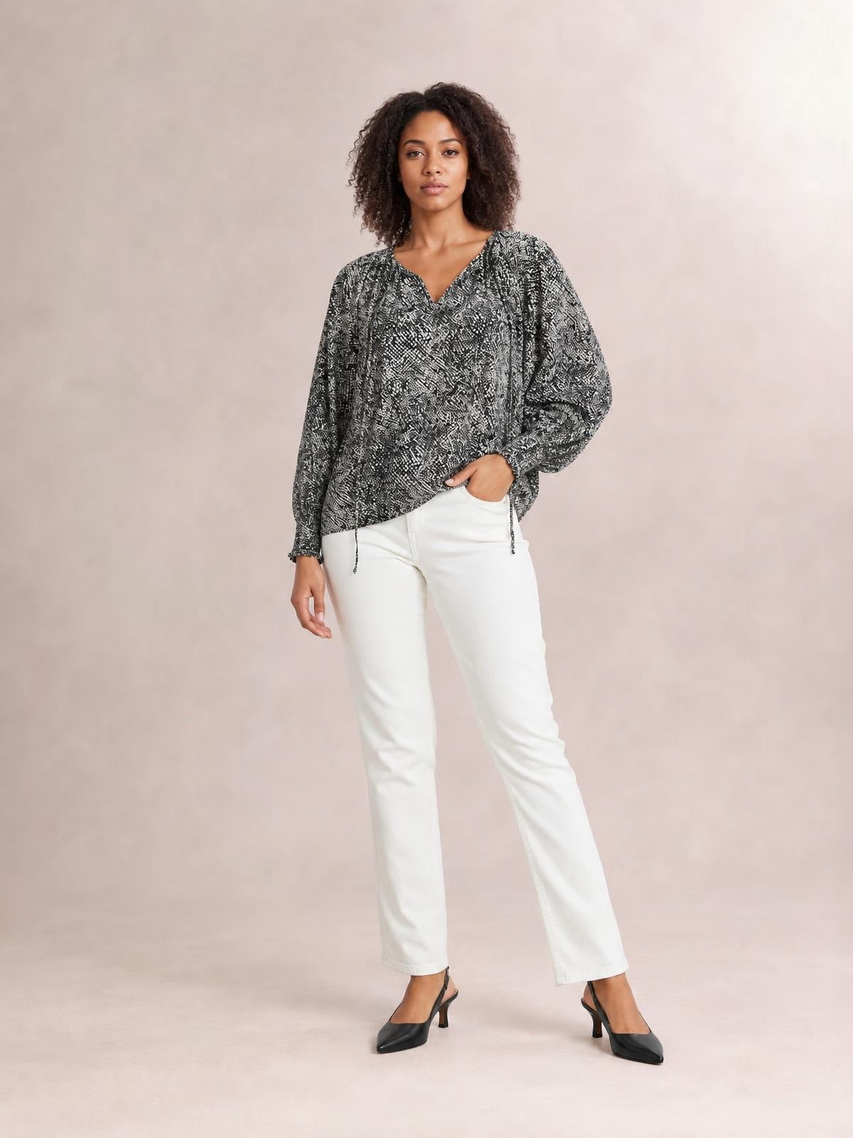 Model poses in a printed black-and-white tie neck blouse with voluminous lantern sleeves, a relaxed silhouette, and gathered cuffs.
