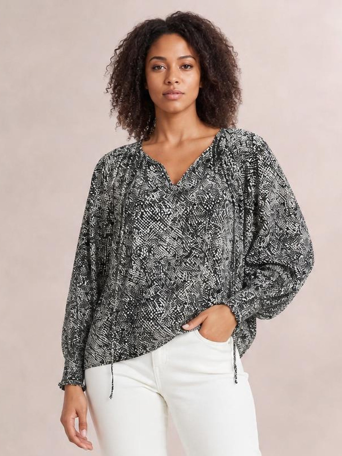 A model stands with one hand in her pocket wearing a black-and-white printed blouse with a relaxed silhouette, V neckline, tied details, and voluminous lantern sleeves.