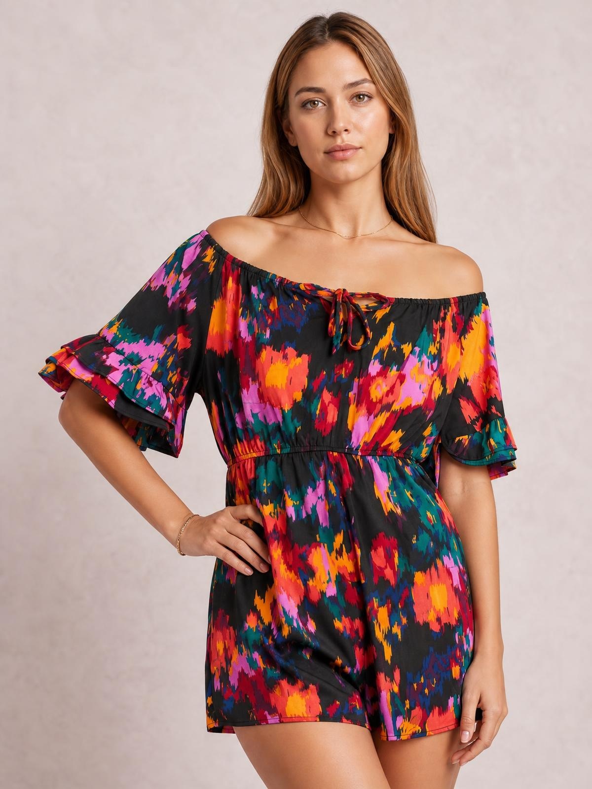 Model poses with one hand on her hip in a multicolored printed romper featuring a tied boat neck, short flounce sleeves, drawstring waist, and shorts-length silhouette.