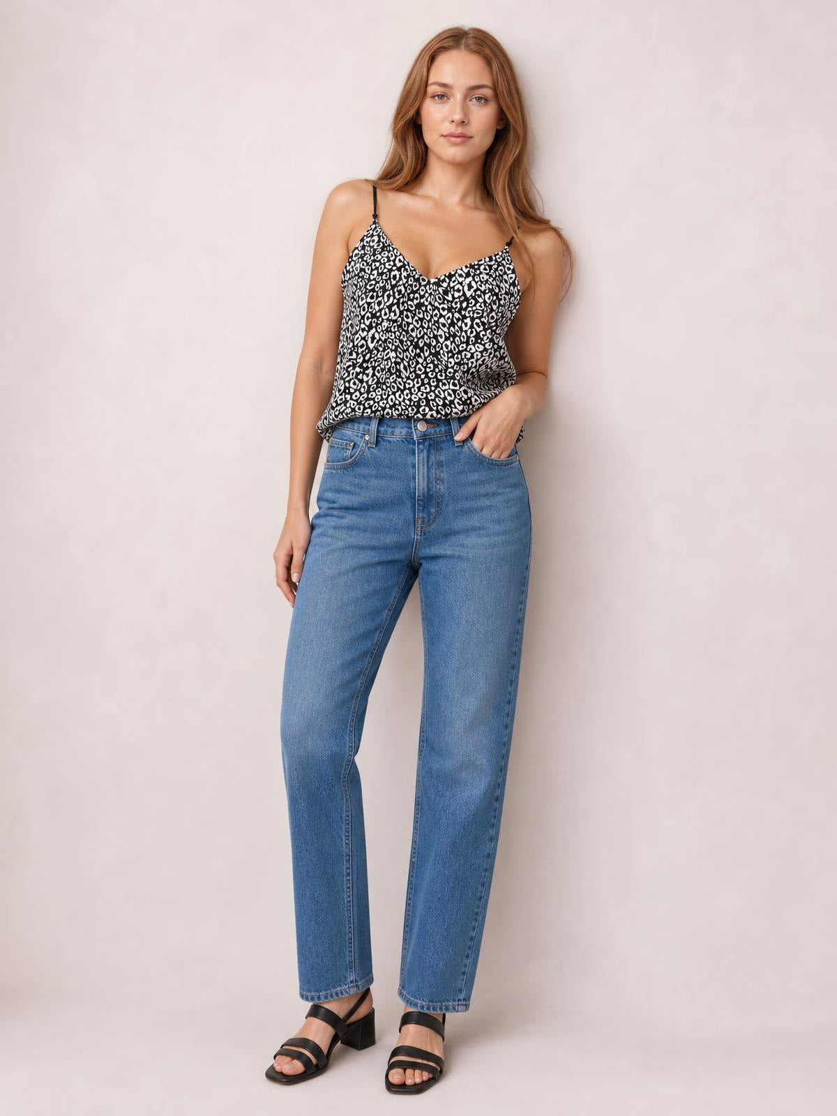 A model poses in a black-and-white printed V-neck cami with slim spaghetti straps and a relaxed silhouette, paired with high-waisted blue jeans.