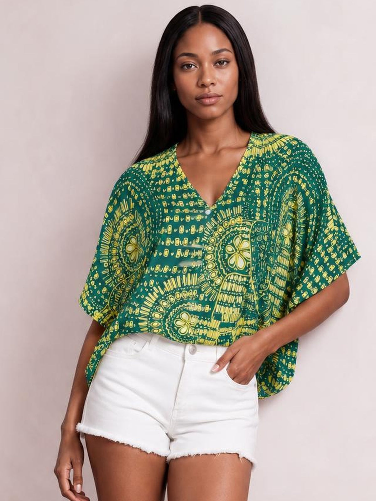 A model wears a green and yellow printed V-neck half-sleeve top with a relaxed silhouette, standing with one hand tucked into her shorts pocket.