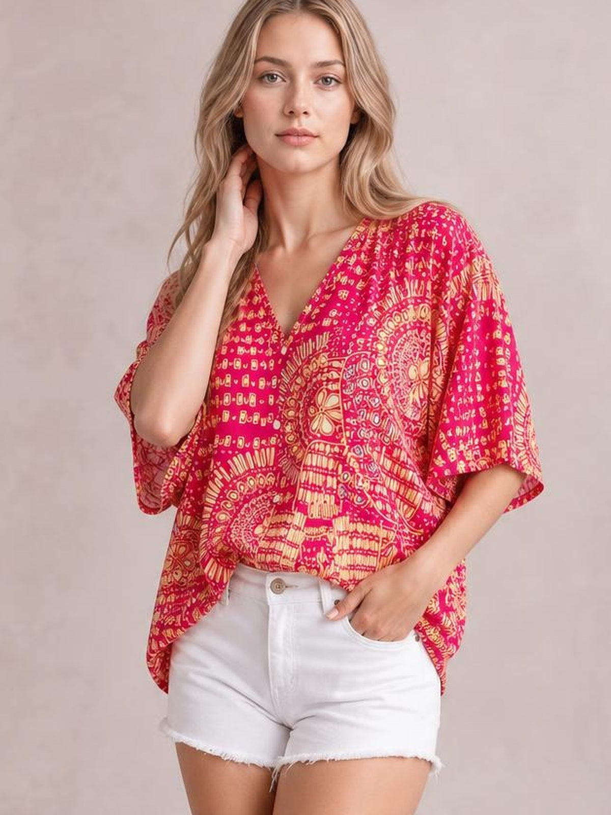 A model poses in a pink printed V-neck half sleeve top with cream abstract motifs, a loose relaxed silhouette, and an easy draped construction.