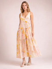 Model wearing a floral printed V-neck sleeveless dress in soft pink, yellow, and green, featuring a gathered waist, tiered flowing ankle-length skirt, and frill detailing.
