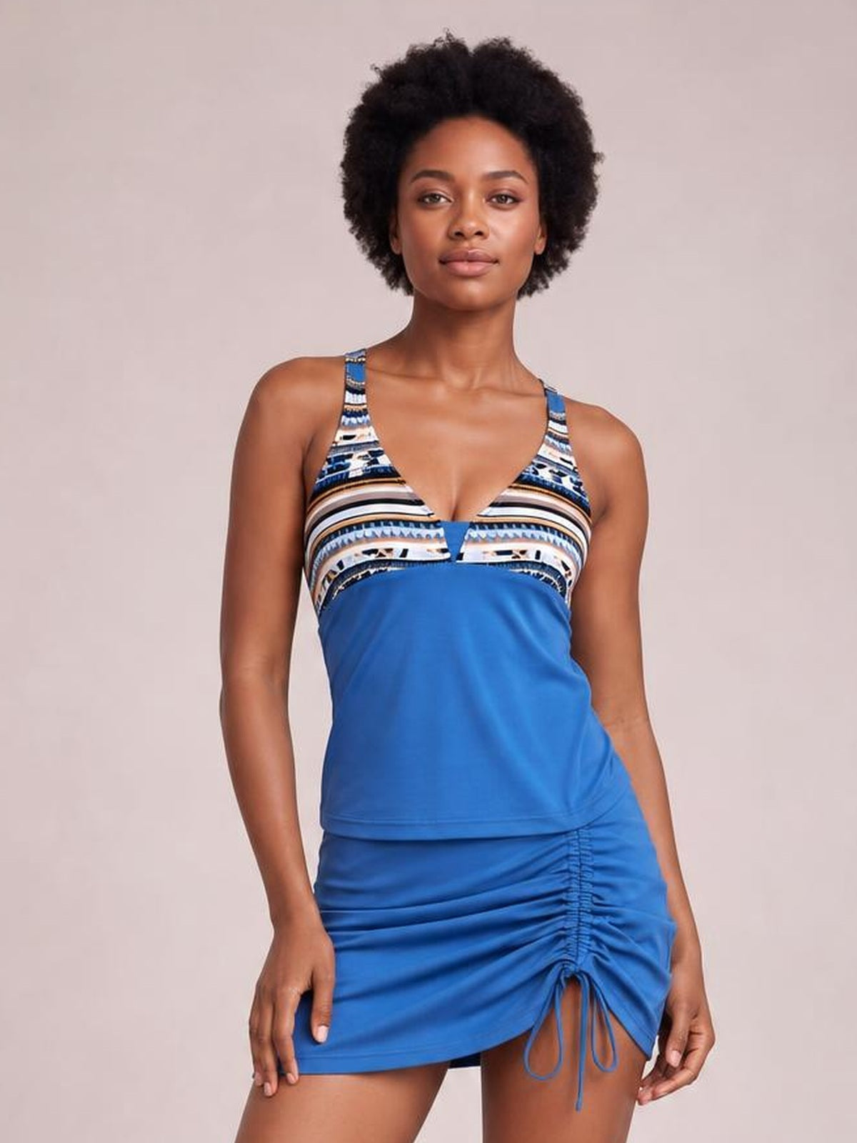 A model stands in a blue printed V-neck tankini with adjustable straps, sleeveless top, and matching ruched drawstring skirt for a fitted two-piece swimsuit silhouette.