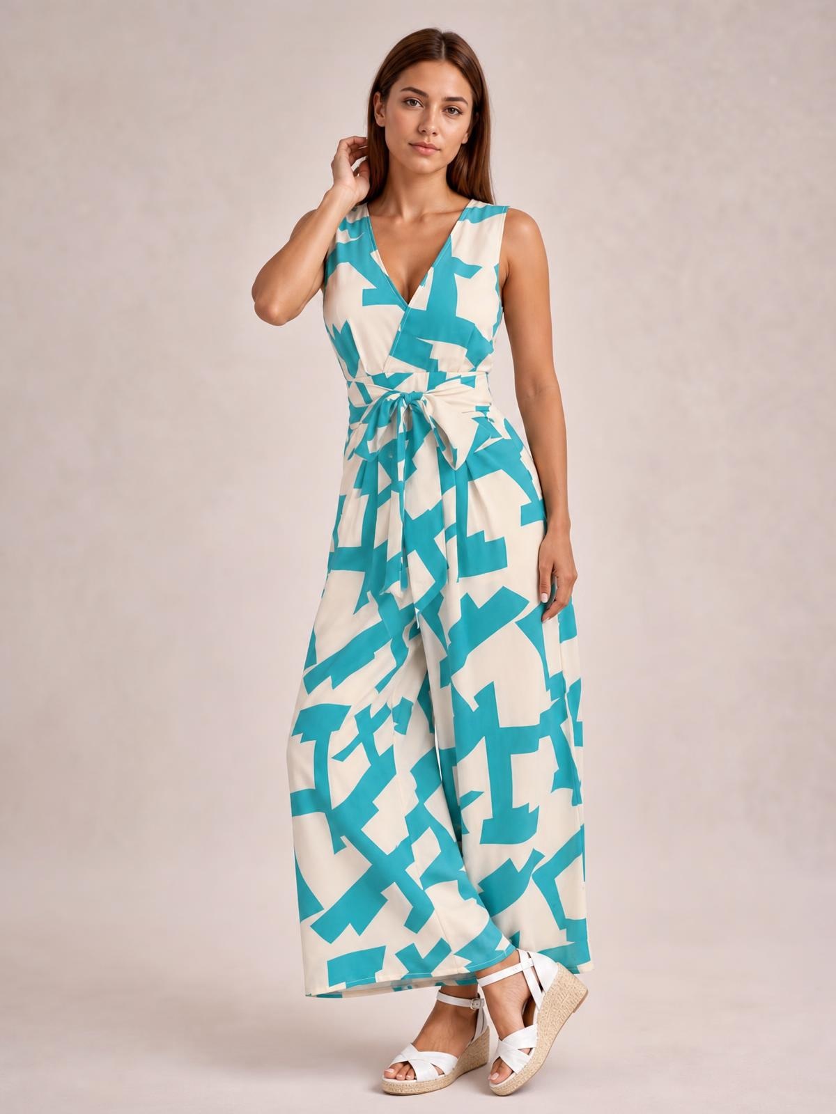 Model poses in a turquoise and cream printed wide-leg jumpsuit with a sleeveless V-neck bodice, tied waist, and flowing full-length silhouette.